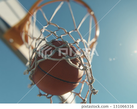Basketball going through net of basketball hoop outdoors under clear blue sky, capturing moment of scoring with sunlight shining brightly 131066316