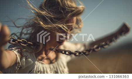 Woman with wind blown hair holding chain in dynamic outdoor scene, conveying strength and freedom, with blurred background of sky and landscape Woman with wind blown hair holding chain in dynamic outdoor scene, conveying strength and freedom, with blurred background of sky and landscape 131066363
