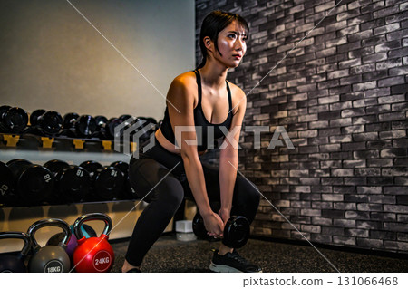 A woman training her buttocks with dumbbell squats. A cool woman exercising at the gym. Hip-up. Muscle training girl. 131066468