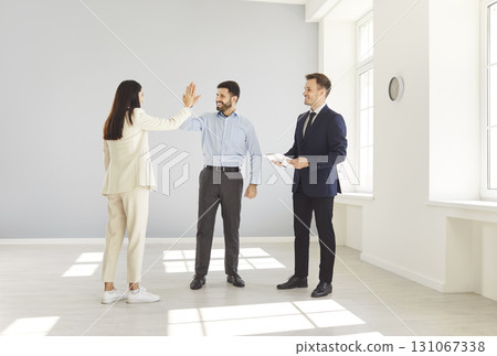 Young couple giving high five each other happy to buy a house standing with smiling man realtor. Young couple giving high five each other happy to buy a house standing with smiling man realtor. 131067338