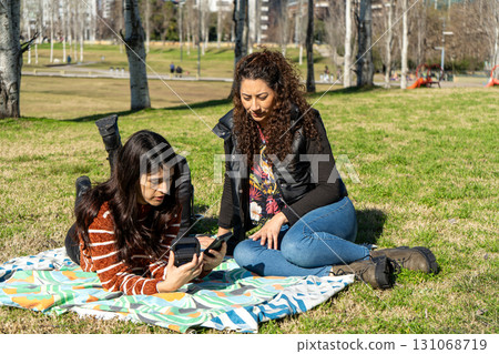 Two latin women using smartphones in park on sunny day 131068719