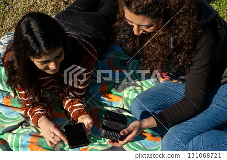 Two women connecting smartphone to portable speaker outdoors 131068721