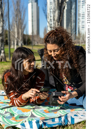Two young women charging smartphone with portable power station in city park Two young women charging smartphone with portable power station in city park 131068722