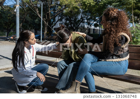 Doctor and friend comforting sad young woman in the park 131068748