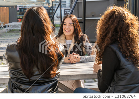 Young women enjoying a conversation at outdoor table Young women enjoying a conversation at outdoor table 131068764