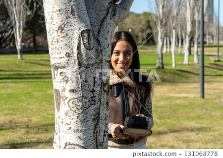University student smiling behind a carved tree in a park on campus University student smiling behind a carved tree in a park on campus 131068778