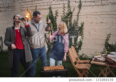 Friends celebrate outdoors with a barbecue and laughter in the evening glow Friends celebrate outdoors with a barbecue and laughter in the evening glow 131069139