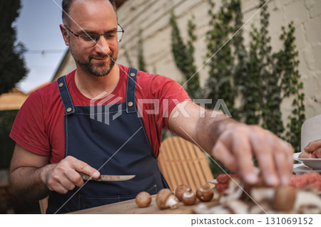 A cheerful man slices mushrooms on a wooden table, enjoying a sunny day A cheerful man slices mushrooms on a wooden table, enjoying a sunny day 131069152