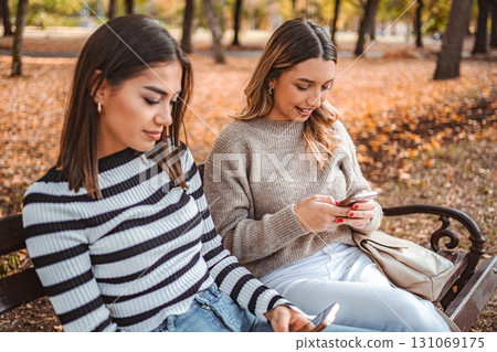 Autumn day in the park with friends enjoying their phones together Autumn day in the park with friends enjoying their phones together 131069175