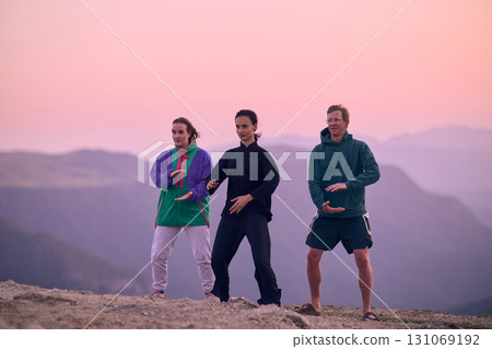 Group of people practicing Tai Chi outdoors at sunrise on mountain, performing slow meditative movements for balance, energy, health, and mindfulness in nature 131069192