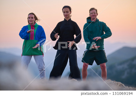 Group of people practicing Tai Chi outdoors at sunrise on mountain, performing slow meditative movements for balance, energy, health, and mindfulness in nature 131069194