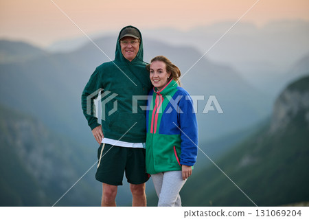 Happy couple posing outdoors on mountain at sunset, dressed in casual colorful hoodies, smiling and enjoying nature, travel, lifestyle, and togetherness in a scenic landscape 131069204