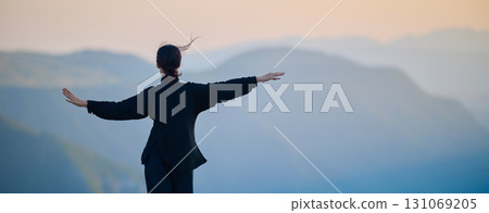 Woman practicing Tai Chi in traditional black outfit on mountain at sunrise, arms outstretched in meditation pose focusing on balance, energy, and mindfulness in nature. 131069205