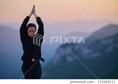 Woman practicing Tai Chi in traditional black outfit on mountain at sunrise, arms outstretched in meditation pose focusing on balance, energy, and mindfulness in nature. Woman practicing Tai Chi in traditional black outfit on mountain at sunrise, arms outstretched in meditation pose focusing on balance, energy, and mindfulness in nature. 131069211