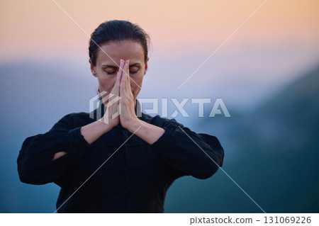 Woman practicing Tai Chi in traditional black outfit on mountain at sunrise, arms outstretched in meditation pose focusing on balance, energy, and mindfulness in nature. Woman practicing Tai Chi in traditional black outfit on mountain at sunrise, arms outstretched in meditation pose focusing on balance, energy, and mindfulness in nature. 131069226