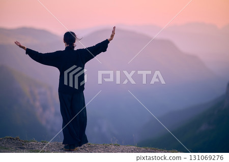 Woman practicing Tai Chi in traditional black outfit on mountain at sunrise, arms outstretched in meditation pose focusing on balance, energy, and mindfulness in nature. Woman practicing Tai Chi in traditional black outfit on mountain at sunrise, arms outstretched in meditation pose focusing on balance, energy, and mindfulness in nature. 131069276