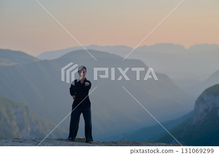 Woman practicing Tai Chi in traditional black outfit on mountain at sunrise, arms outstretched in meditation pose focusing on balance, energy, and mindfulness in nature. Woman practicing Tai Chi in traditional black outfit on mountain at sunrise, arms outstretched in meditation pose focusing on balance, energy, and mindfulness in nature. 131069299