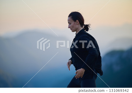 Woman practicing Tai Chi in traditional black outfit on mountain at sunrise, arms outstretched in meditation pose focusing on balance, energy, and mindfulness in nature. 131069342