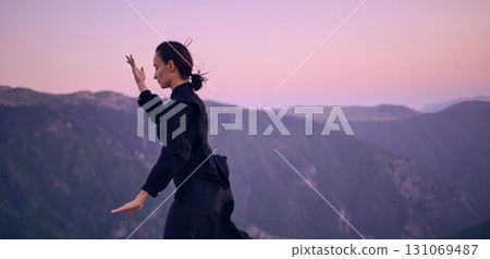 Woman practicing Tai Chi in traditional black outfit on mountain at sunrise, arms outstretched in meditation pose focusing on balance, energy, and mindfulness in nature. Woman practicing Tai Chi in traditional black outfit on mountain at sunrise, arms outstretched in meditation pose focusing on balance, energy, and mindfulness in nature. 131069487