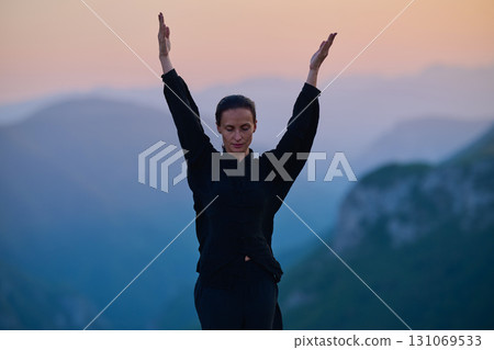 Woman practicing Tai Chi in traditional black outfit on mountain at sunrise, arms outstretched in meditation pose focusing on balance, energy, and mindfulness in nature. Woman practicing Tai Chi in traditional black outfit on mountain at sunrise, arms outstretched in meditation pose focusing on balance, energy, and mindfulness in nature. 131069533