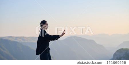 Woman practicing Tai Chi in traditional black outfit on mountain at sunrise, arms outstretched in meditation pose focusing on balance, energy, and mindfulness in nature. Woman practicing Tai Chi in traditional black outfit on mountain at sunrise, arms outstretched in meditation pose focusing on balance, energy, and mindfulness in nature. 131069636