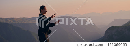 Woman practicing Tai Chi in traditional black outfit on mountain at sunrise, arms outstretched in meditation pose focusing on balance, energy, and mindfulness in nature. 131069663