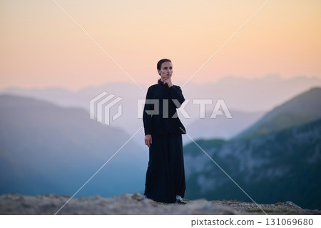 Woman practicing Tai Chi in traditional black outfit on mountain at sunrise, arms outstretched in meditation pose focusing on balance, energy, and mindfulness in nature. 131069680