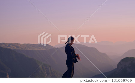 Woman practicing Tai Chi in traditional black outfit on mountain at sunrise, arms outstretched in meditation pose focusing on balance, energy, and mindfulness in nature. 131069709