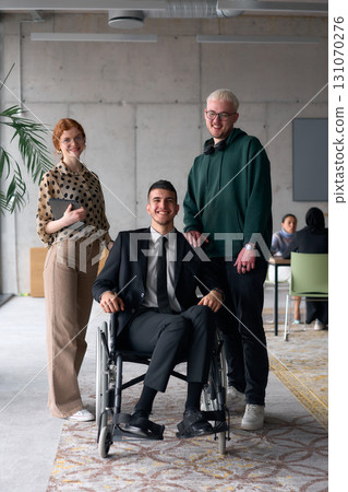 Group cheerful business colleagues, including a businessman in a wheelchair, posing together in a modern office, showcasing teamwork and inclusivity 131070276