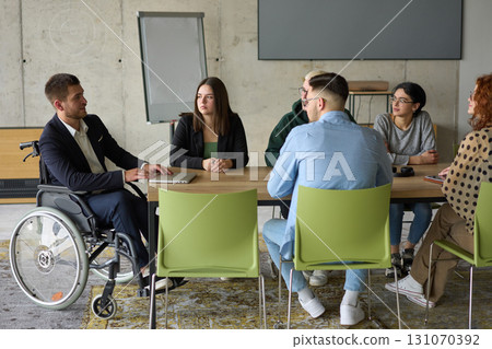 A diverse group of business professionals sitting in an office meeting with their director, who is in a wheelchair, fostering collaboration, leadership, and inclusivity 131070392