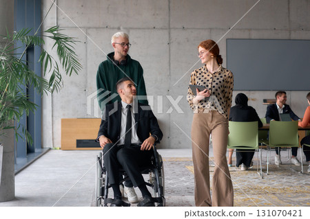 A diverse team of business colleagues, including a director in a wheelchair, engages in a collaborative discussion as they move together through a modern office space A diverse team of business colleagues, including a director in a wheelchair, engages in a collaborative discussion as they move together through a modern office space 131070421