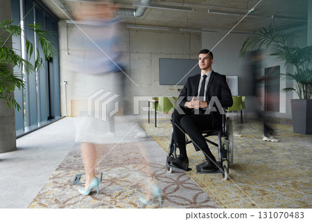 A businessman in a wheelchair navigating through a busy office, surrounded by his colleagues who are actively engaged in their work and collaboration 131070483
