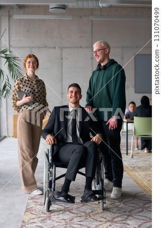 Group cheerful business colleagues, including a businessman in a wheelchair, posing together in a modern office, showcasing teamwork and inclusivity 131070499