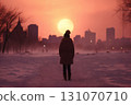 a someone is walking along trail in snowy city park, in the distance of the sunset over the houses, winter season, it's cold and a blizzard 131070710