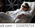 portrait of a fashionable man relaxing in a white armchair 131070714