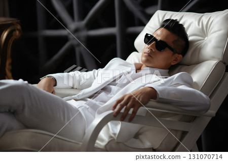 portrait of a fashionable man relaxing in a white armchair 131070714
