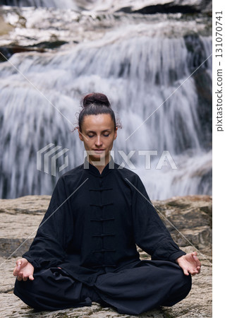 A woman sits in lotus pose, practicing yoga and tai chi under a tropical waterfall, meditating with calm strength and mindfulness, fully connected to the energy of nature, tranquility and inner A woman sits in lotus pose, practicing yoga and tai chi under a tropical waterfall, meditating with calm strength and mindfulness, fully connected to the energy of nature, tranquility and inner 131070741