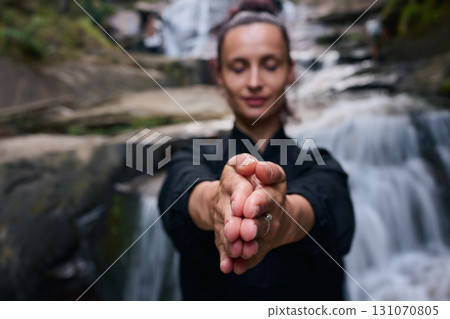Woman practicing Tai Chi in nature, wearing a traditional black martial arts uniform, standing gracefully near a waterfall, focused on meditation and balance. Healthy lifestyle in asian culture Woman practicing Tai Chi in nature, wearing a traditional black martial arts uniform, standing gracefully near a waterfall, focused on meditation and balance. Healthy lifestyle in asian culture 131070805
