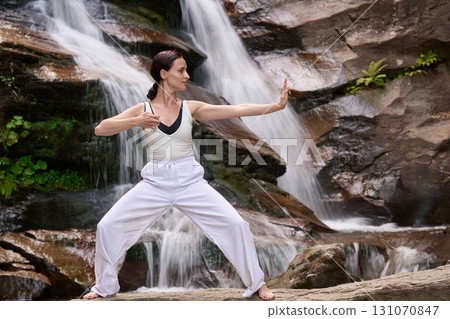 woman performing slow tai chi movements near a waterfall and river at sunset capturing harmony balance and fitness in nature woman performing slow tai chi movements near a waterfall and river at sunset capturing harmony balance and fitness in nature 131070847