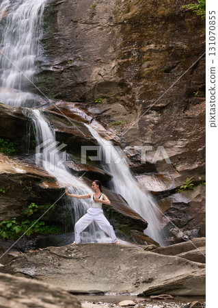 woman performing slow tai chi movements near a waterfall and river at sunset capturing harmony balance and fitness in nature 131070855