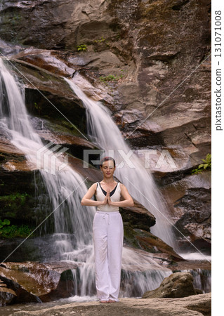 woman performing slow tai chi movements near a waterfall and river at sunset capturing harmony balance and fitness in nature 131071008