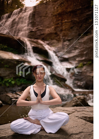 Young woman sitting in lotus pose under tropical waterfall meditating with calm strength and mindfulness fully connected to nature energy tranquility and inner balance 131071127