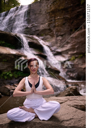 Young woman sitting in lotus pose under tropical waterfall meditating with calm strength and mindfulness fully connected to nature energy tranquility and inner balance 131071237