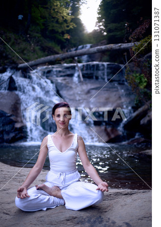 Young woman sitting in lotus pose under tropical waterfall meditating with calm strength and mindfulness fully connected to nature energy tranquility and inner balance Young woman sitting in lotus pose under tropical waterfall meditating with calm strength and mindfulness fully connected to nature energy tranquility and inner balance 131071387