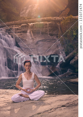 Young woman sitting in lotus pose under tropical waterfall meditating with calm strength and mindfulness fully connected to nature energy tranquility and inner balance Young woman sitting in lotus pose under tropical waterfall meditating with calm strength and mindfulness fully connected to nature energy tranquility and inner balance 131071474