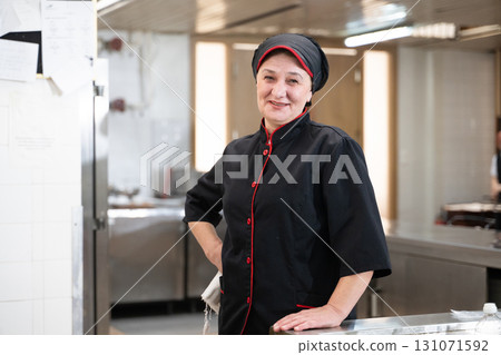 Portrait of a female chef in a black uniform with red details smiling in a professional restaurant kitchen. Image highlights hospitality staff, confidence, and culinary professionalism. Portrait of a female chef in a black uniform with red details smiling in a professional restaurant kitchen. Image highlights hospitality staff, confidence, and culinary professionalism. 131071592