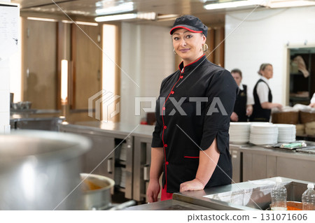 Portrait of a female chef in a black uniform with red details smiling in a professional restaurant kitchen. Image highlights hospitality staff, confidence, and culinary professionalism. Portrait of a female chef in a black uniform with red details smiling in a professional restaurant kitchen. Image highlights hospitality staff, confidence, and culinary professionalism. 131071606