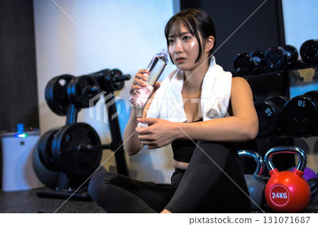 A woman taking a break while drinking water from a plastic bottle. A cool woman exercising at the gym. Trimmed up. A woman taking a break while drinking water from a plastic bottle. A cool woman exercising at the gym. Trimmed up. 131071687