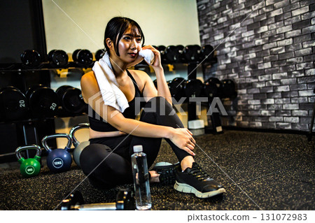 A woman taking a break and wiping sweat with a towel. A cool woman exercising at the gym. A woman taking a break and wiping sweat with a towel. A cool woman exercising at the gym. 131072983