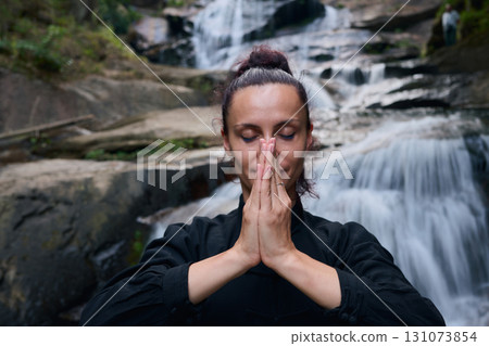 Woman practicing Tai Chi in nature, wearing a traditional black martial arts uniform, standing gracefully near a waterfall, focused on meditation and balance. Healthy lifestyle in asian culture Woman practicing Tai Chi in nature, wearing a traditional black martial arts uniform, standing gracefully near a waterfall, focused on meditation and balance. Healthy lifestyle in asian culture 131073854
